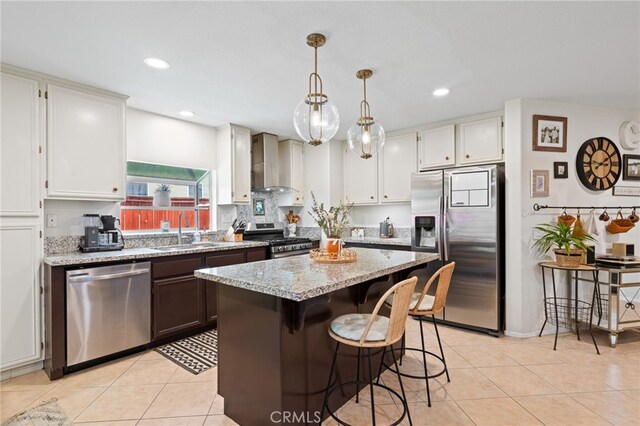 kitchen with a kitchen island, wall chimney exhaust hood, a sink, light tile patterned floors, and stainless steel appliances
