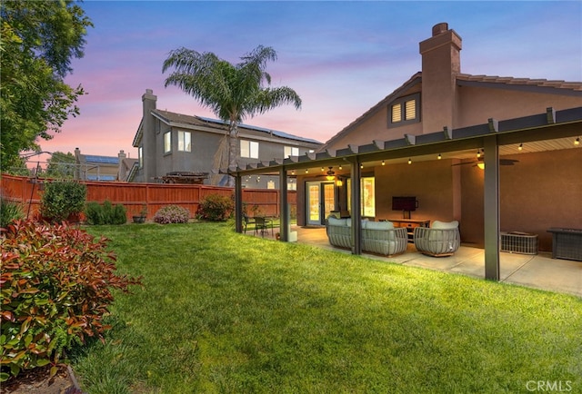 yard at dusk with a fenced backyard, a ceiling fan, and a patio area