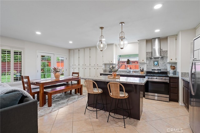 kitchen featuring a healthy amount of sunlight, wall chimney range hood, a center island, recessed lighting, and appliances with stainless steel finishes