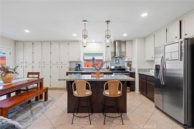 kitchen featuring wall chimney range hood, appliances with stainless steel finishes, light tile patterned floors, and a center island