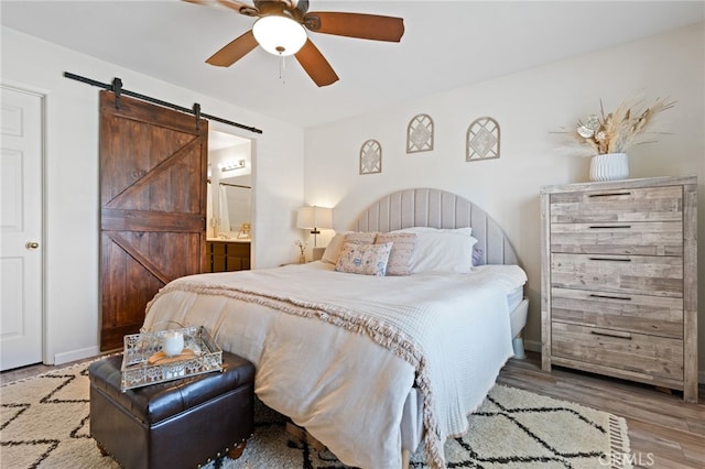 bedroom featuring a ceiling fan, a barn door, wood finished floors, and ensuite bath