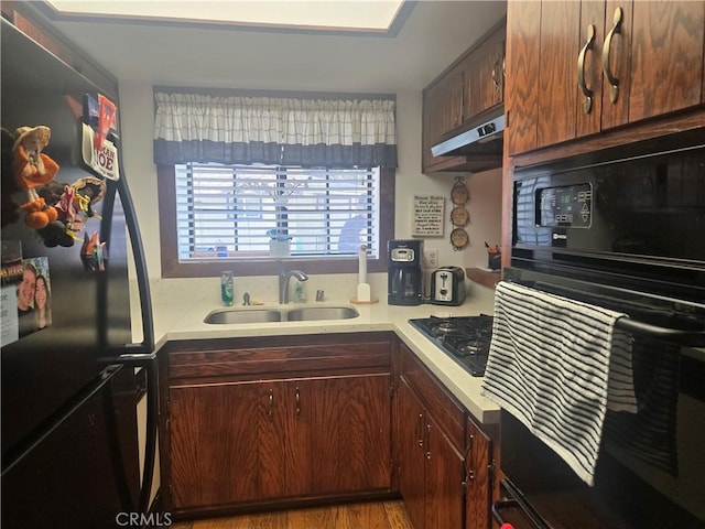 kitchen featuring black appliances, light countertops, under cabinet range hood, and a sink