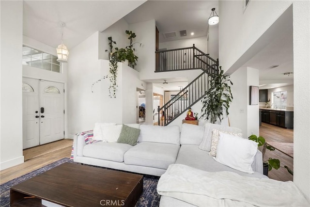 living room with stairway, visible vents, baseboards, wood finished floors, and a high ceiling