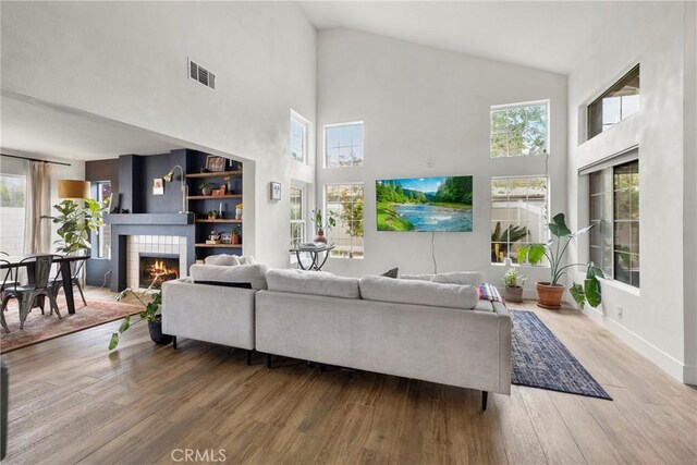 living room with wood finished floors, a tile fireplace, baseboards, visible vents, and high vaulted ceiling