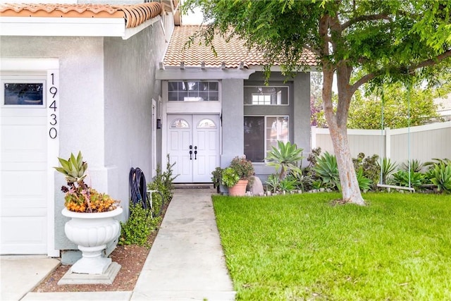 view of exterior entry with fence, stucco siding, a tiled roof, and a lawn