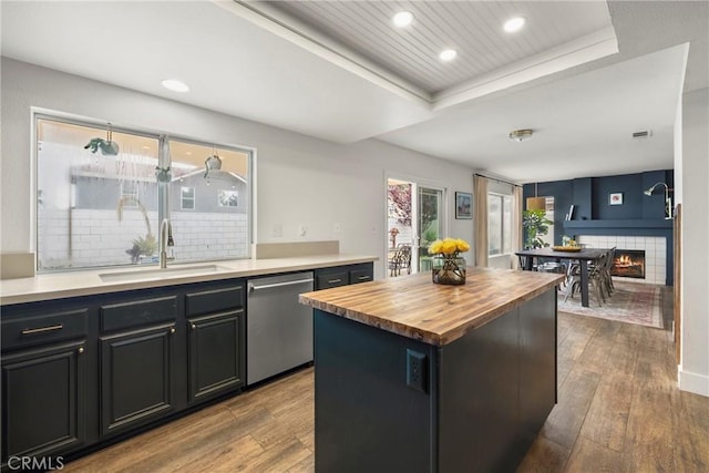 kitchen with wood finished floors, butcher block counters, dishwasher, a sink, and a raised ceiling