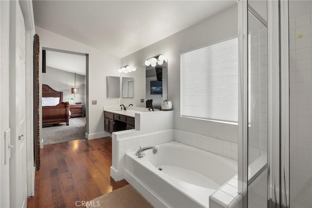 bathroom featuring hardwood / wood-style floors, a bath, vanity, baseboards, and lofted ceiling