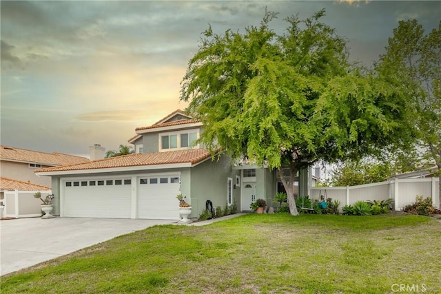 view of front of home featuring a tile roof, a lawn, driveway, stucco siding, and fence