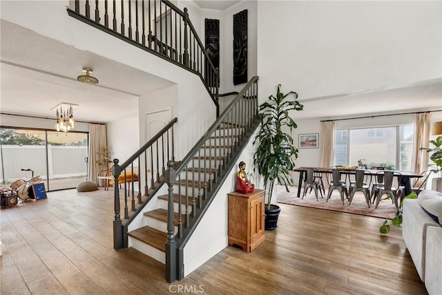 stairs with wood finished floors, a healthy amount of sunlight, a high ceiling, and a notable chandelier