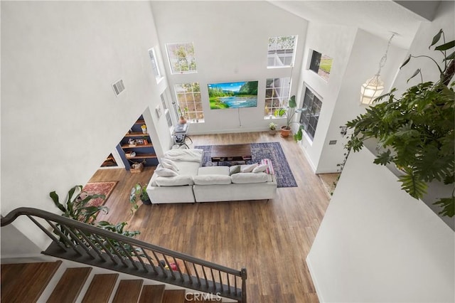 living room with stairway, visible vents, baseboards, a towering ceiling, and wood finished floors