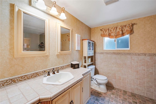 bathroom with tile walls, wallpapered walls, toilet, and vanity