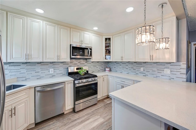 kitchen featuring appliances with stainless steel finishes, light wood finished floors, decorative light fixtures, a notable chandelier, and backsplash