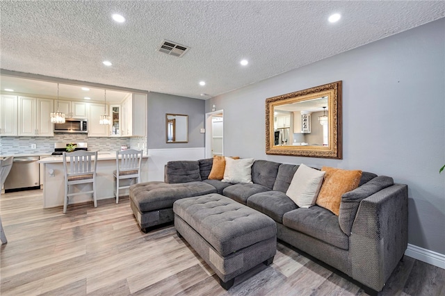 living room featuring a textured ceiling, visible vents, recessed lighting, and light wood-style flooring