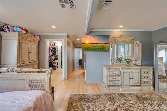 bedroom featuring a walk in closet, visible vents, ornamental molding, and light wood-style floors