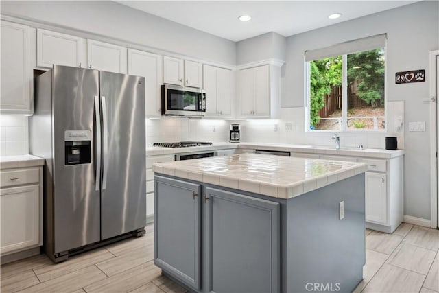 kitchen featuring stainless steel appliances, tile counters, white cabinetry, and a sink