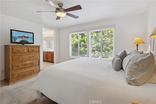 bedroom featuring light colored carpet, baseboards, ceiling fan, and ensuite bath