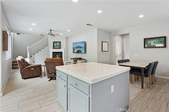 kitchen featuring wood finish floors, tile countertops, open floor plan, baseboards, and visible vents