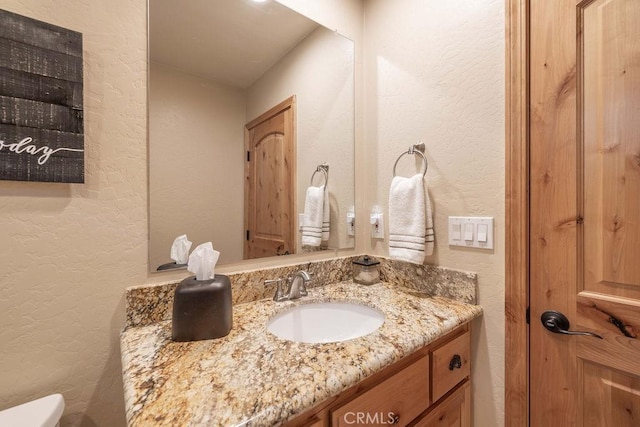 bathroom with toilet, a textured wall, and vanity