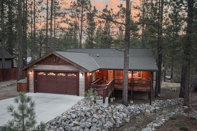 chalet / cabin featuring a wooden deck, a garage, stone siding, roof with shingles, and concrete driveway