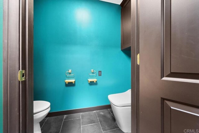 half bath featuring baseboards, tile patterned floors, and toilet