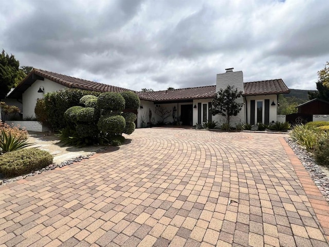 mediterranean / spanish-style house featuring stucco siding, a chimney, a tiled roof, and curved driveway
