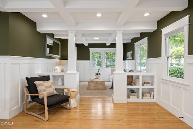 living area featuring coffered ceiling, a decorative wall, beamed ceiling, and decorative columns