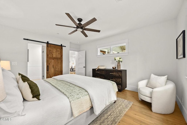 bedroom with baseboards, a ceiling fan, light wood finished floors, and a barn door