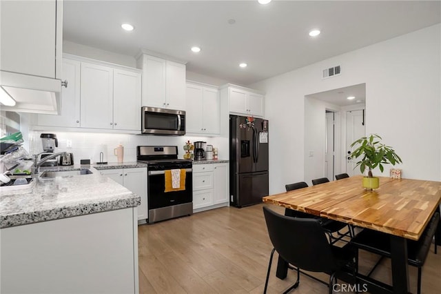 kitchen featuring light wood-style flooring, stainless steel appliances, a sink, white cabinetry, and visible vents