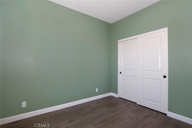 unfurnished bedroom with dark wood finished floors, a closet, and baseboards