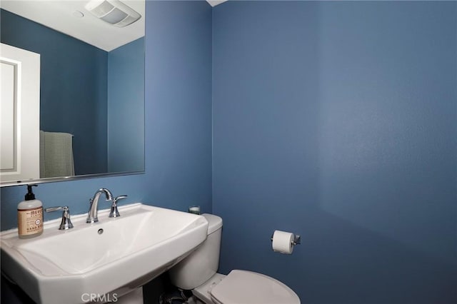 half bath with visible vents, toilet, and a sink