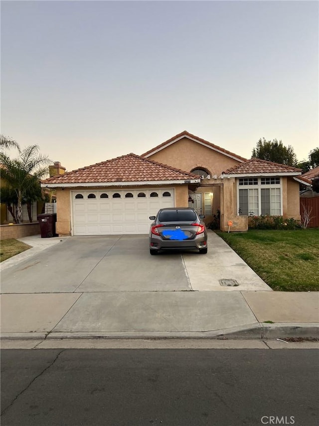 mediterranean / spanish home featuring stucco siding, concrete driveway, a lawn, and a garage