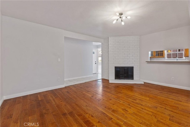 unfurnished living room featuring a brick fireplace, baseboards, and wood finished floors