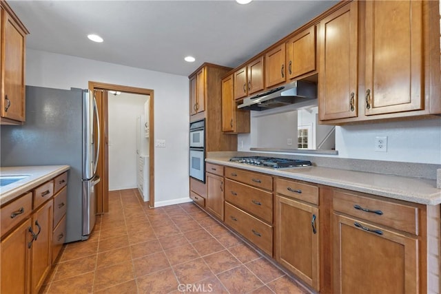kitchen featuring brown cabinetry, recessed lighting, light countertops, under cabinet range hood, and appliances with stainless steel finishes
