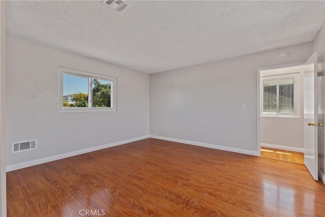 spare room with baseboards, a textured ceiling, visible vents, and wood finished floors