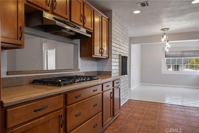 kitchen with dark tile patterned floors, visible vents, brown cabinets, stainless steel gas stovetop, and under cabinet range hood