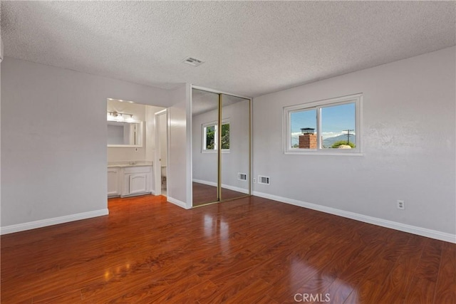 unfurnished bedroom featuring a textured ceiling, visible vents, wood finished floors, baseboards, and a closet