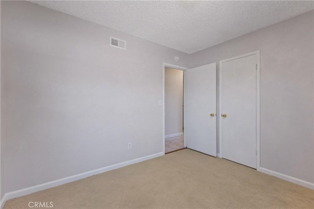 unfurnished bedroom featuring visible vents, a textured ceiling, baseboards, and light carpet