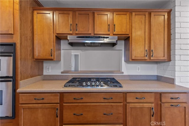 kitchen with brown cabinetry, light countertops, range hood, and stainless steel appliances