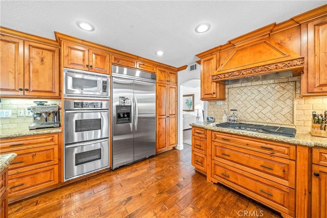 kitchen with arched walkways, built in appliances, backsplash, visible vents, and dark wood-type flooring