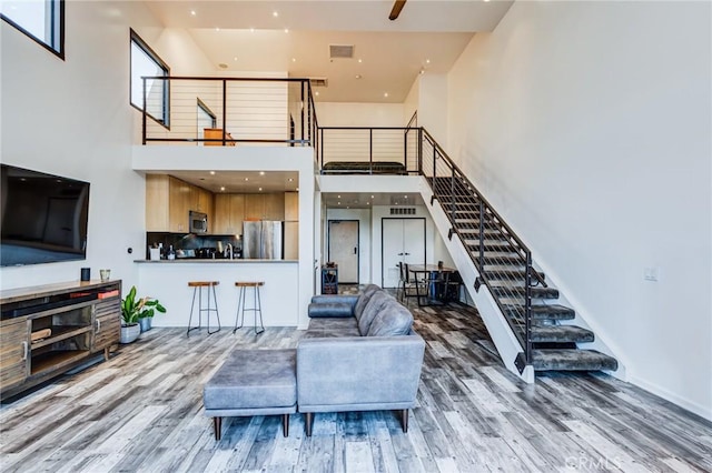 living room featuring wood finished floors, visible vents, stairs, and a high ceiling