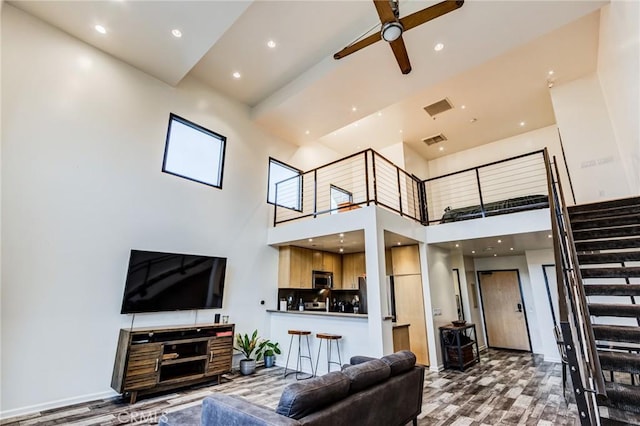 living room with ceiling fan, stairs, visible vents, a towering ceiling, and wood finished floors