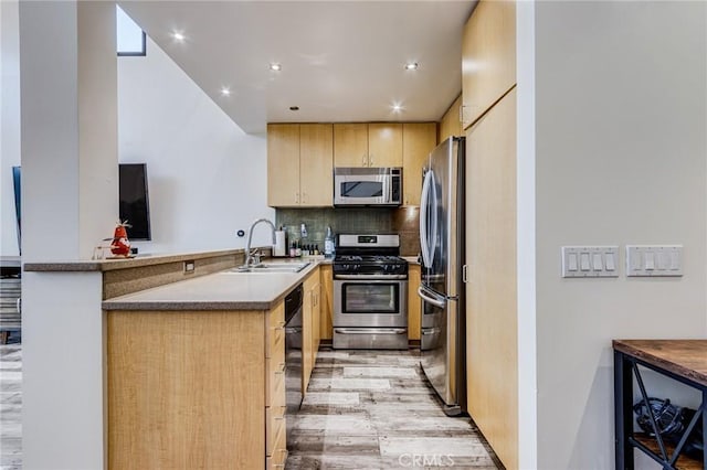 kitchen with a sink, light wood-style floors, light brown cabinets, stainless steel appliances, and a peninsula