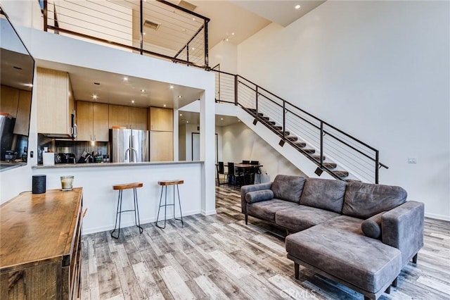 living area with recessed lighting, light wood finished floors, stairs, and a high ceiling