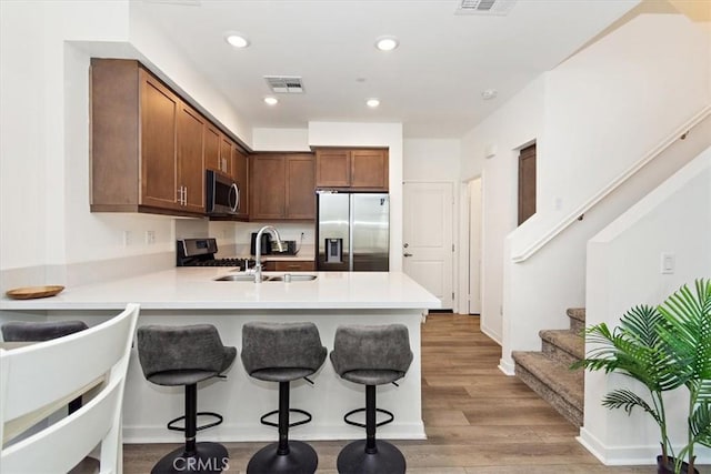 1353 Clary Ct, Upland, CA 91786 - kitchen with appliances with stainless steel finishes, a sink, a peninsula, a kitchen bar, and light wood-type flooring