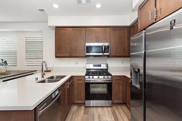kitchen featuring a peninsula, light countertops, a sink, light wood-style flooring, and appliances with stainless steel finishes