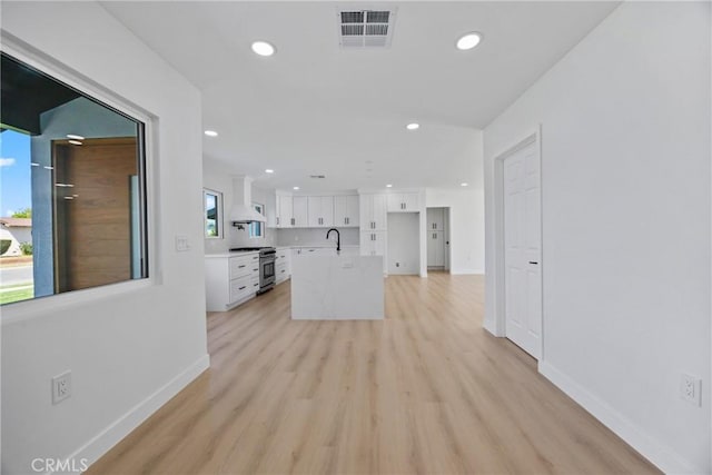 kitchen with a sink, high end range, light wood-style floors, visible vents, and white cabinets