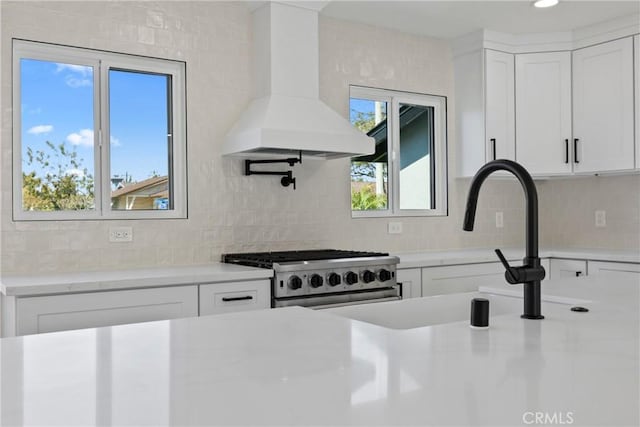 kitchen featuring gas stove, decorative backsplash, light countertops, and premium range hood