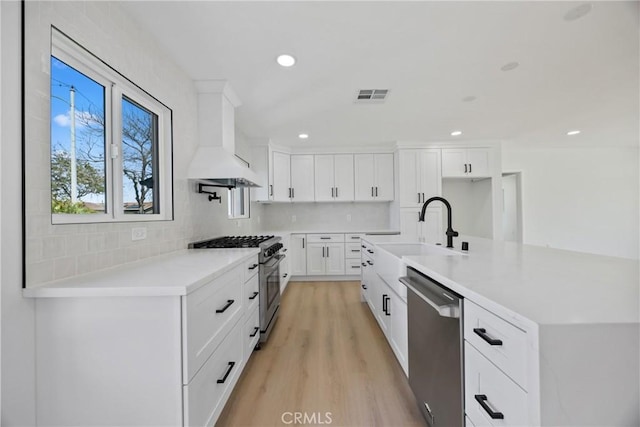 kitchen with tasteful backsplash, custom range hood, a sink, appliances with stainless steel finishes, and visible vents