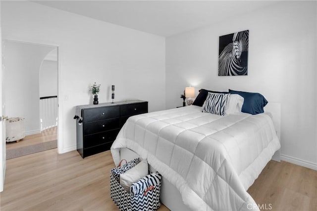 bedroom featuring baseboards, arched walkways, and light wood-style flooring
