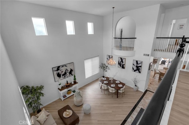 living area featuring a notable chandelier, visible vents, wood finished floors, and a towering ceiling